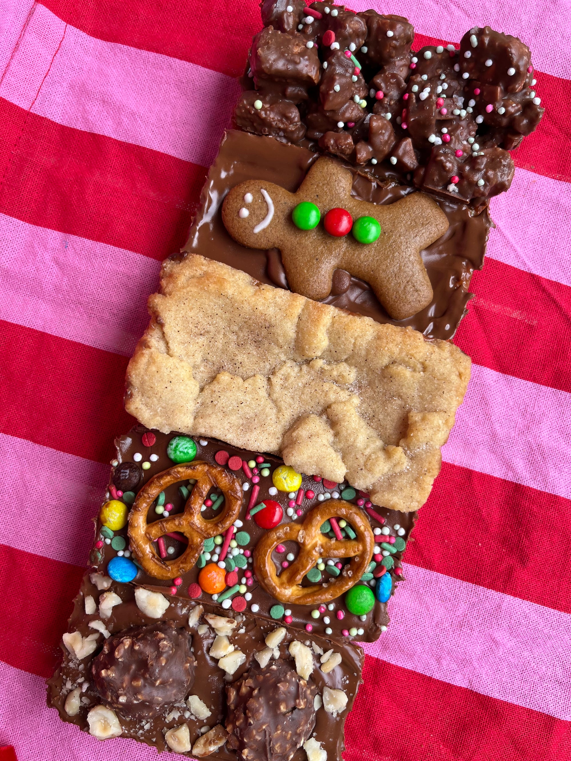 Assorted caramel slices including a gingerbread, rocky road, snickerdoodle, christmas crack and Ferrero Rocher on a striped red and pink background.